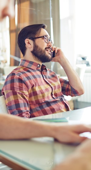 An image of a young, bearded professional on the phone. Probably calling a client to provide fantastic customer service while reminding them of a payment deadline coming up.