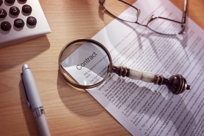 Contract lying on desk with a magnifying glass emphasizing the word 'contract'. The importance of a signed contract in client work cannot be overstated.